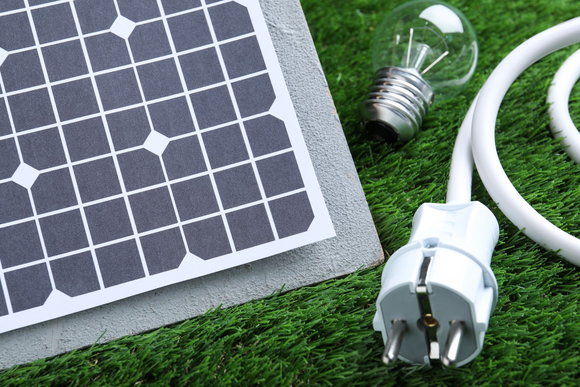 Solar panel, cable and light bulb on green grass, closeup